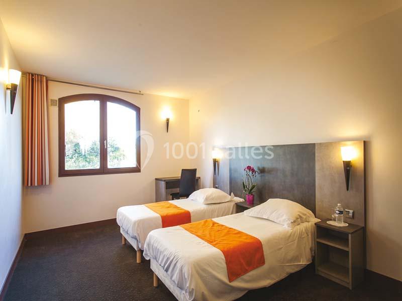 Deux lits simples avec couvre-lits orange dans une chambre lumineuse, équipée d'un bureau et d'une fenêtre avec vue.