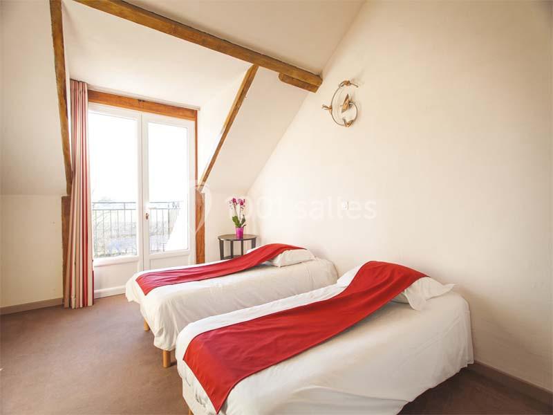 Deux lits simples avec couvre-lits rouges dans une chambre lumineuse avec poutres apparentes et une porte-fenêtre.