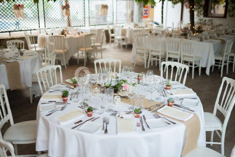 Salle de réception décorée avec des tables rondes dressées, nappes blanches, vaisselle élégante et centres de table fleuris.