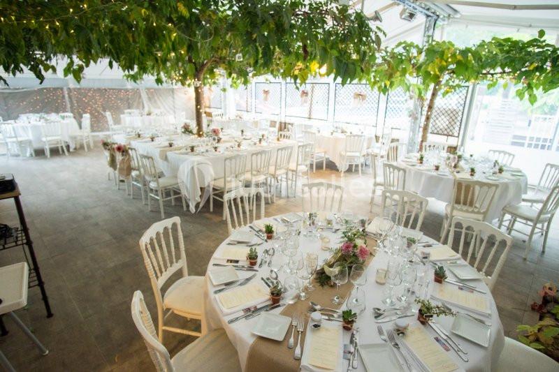 Salle décorée pour un mariage avec des tables rondes dressées, nappes blanches et centres de table fleuris.