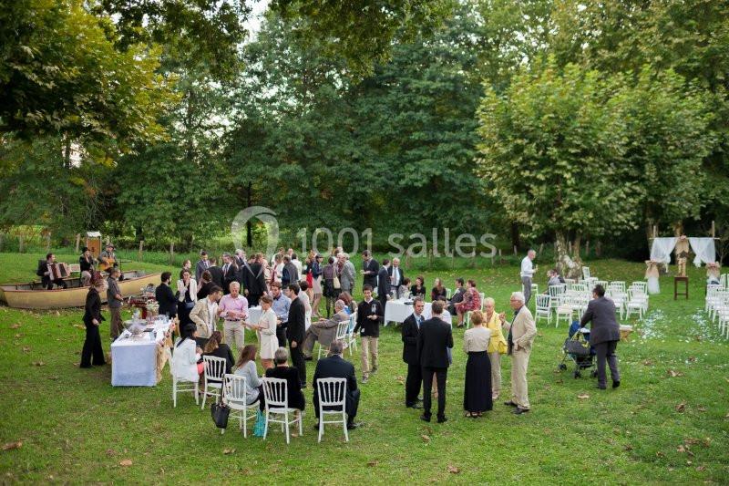 Groupe de personnes rassemblées dans un jardin verdoyant, avec des chaises blanches et une table de buffet à proximité.