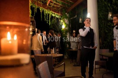 Groupe de personnes discutant sur une terrasse éclairée, entourée de végétation et de bougies.