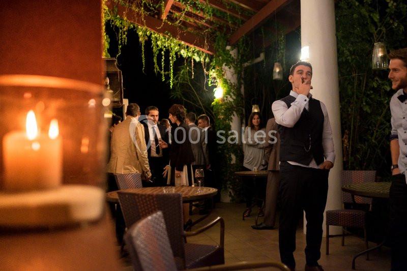 Groupe de personnes discutant sur une terrasse éclairée, entourée de végétation et de bougies.