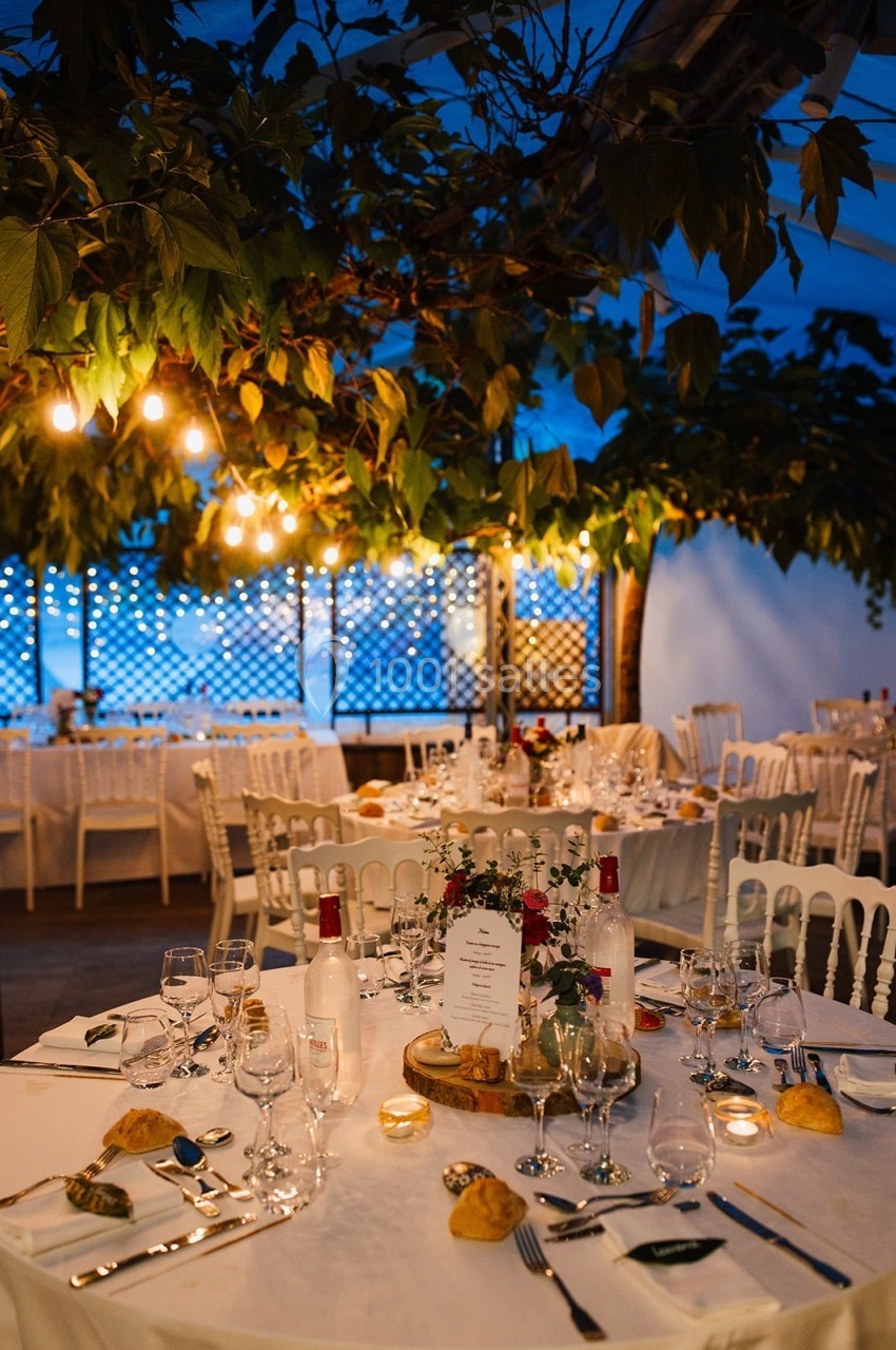 Salle de réception décorée avec des tables dressées, éclairage chaleureux et feuillage suspendu.