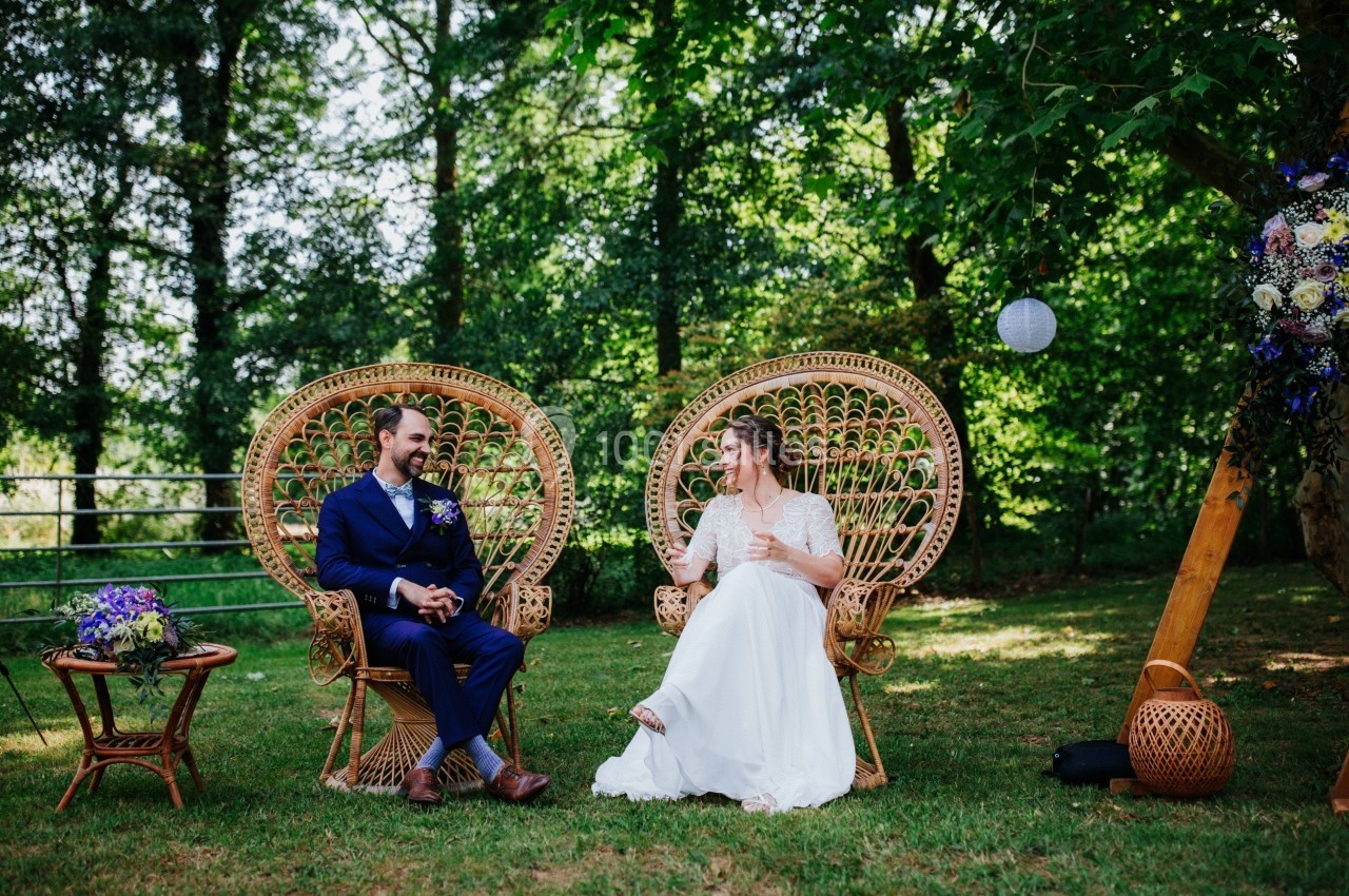 Un couple assis sur des fauteuils en rotin dans un jardin verdoyant, entouré de décorations florales.
