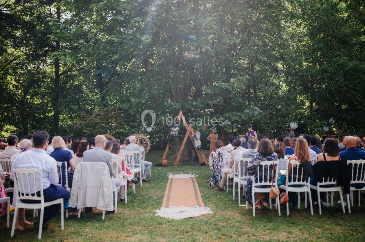 Cérémonie en plein air avec des invités assis, un autel décoré et une allée centrale dans un cadre boisé.