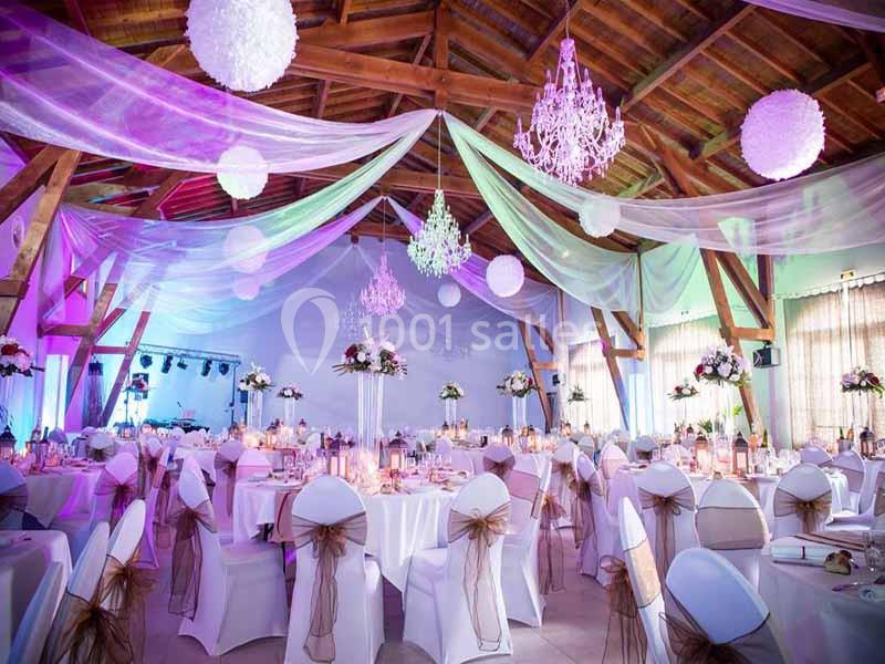 Salle de réception décorée avec des tables dressées, des chaises blanches ornées de nœuds et des guirlandes lumineuses…