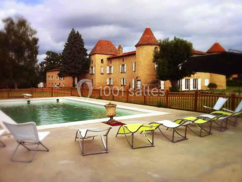 Piscine extérieure entourée de chaises longues devant un bâtiment en pierre avec des toits en tuiles rouges.