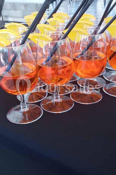 Verres de cocktail orange garnis de tranches d'orange et de pailles noires, disposés sur une nappe noire.