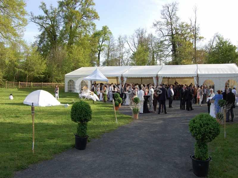 Groupe de personnes rassemblées près d'une grande tente blanche dans un parc verdoyant par une journée ensoleillée.