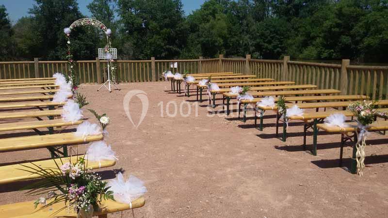 Bancs en bois décorés de fleurs et rubans blancs, disposés en extérieur pour une cérémonie, avec une arche florale au fond.
