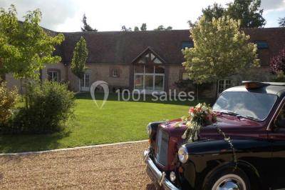 Salle de réception lumineuse avec tables rondes décorées, chaises blanches et poutres apparentes en bois.