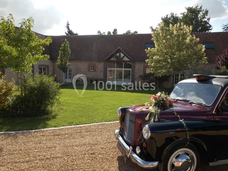 Un taxi noir décoré de fleurs est garé devant une maison en pierre avec un jardin verdoyant.