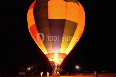 Salle de réception lumineuse avec tables rondes décorées, chaises blanches et poutres apparentes en bois.