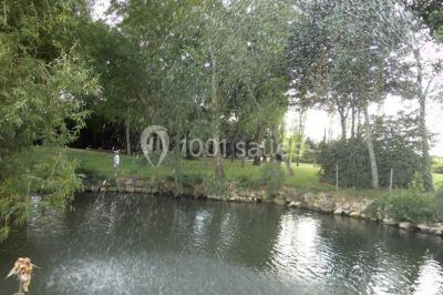 Salle de réception lumineuse avec tables rondes décorées, chaises blanches et poutres apparentes en bois.