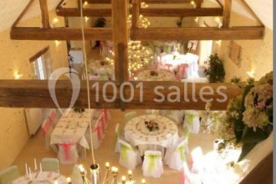 Salle de réception lumineuse avec tables rondes décorées, chaises blanches et poutres apparentes en bois.