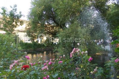 Salle de réception lumineuse avec tables rondes décorées, chaises blanches et poutres apparentes en bois.