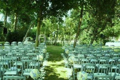 Salle de réception lumineuse avec tables rondes décorées, chaises blanches et poutres apparentes en bois.