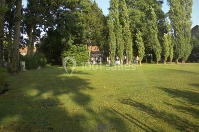Salle de réception lumineuse avec tables rondes décorées, chaises blanches et poutres apparentes en bois.