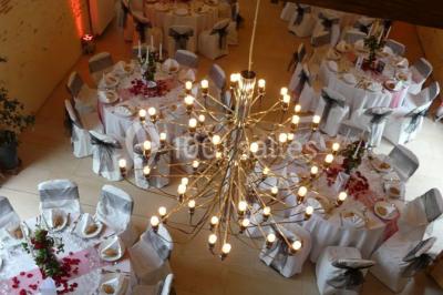 Salle de réception lumineuse avec tables rondes décorées, chaises blanches et poutres apparentes en bois.