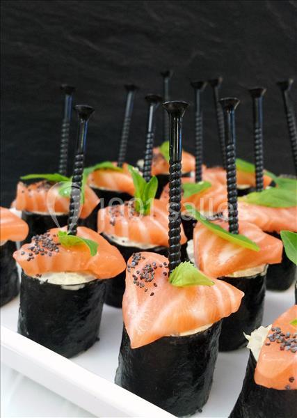 Sushis au saumon garnis de graines de pavot et de feuilles vertes, présentés avec des pics noirs sur un plateau blanc.