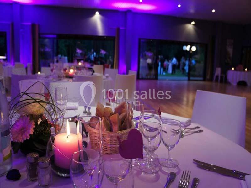 Salle de réception décorée avec des tables dressées, éclairage violet et vue sur l'extérieur à travers de grandes baies…
