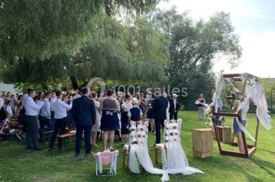 Table en bois décorée de bougies, fleurs et feuillage, entourée de chaises, sous une arche végétale dans une salle lumineuse.