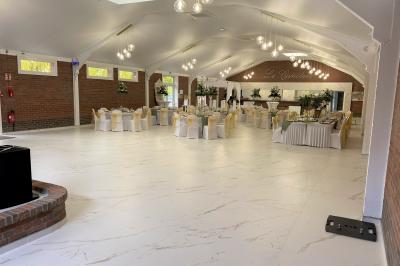 Table en bois décorée de bougies, fleurs et feuillage, entourée de chaises, sous une arche végétale dans une salle lumineuse.