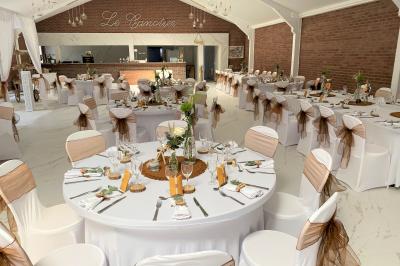 Table en bois décorée de bougies, fleurs et feuillage, entourée de chaises, sous une arche végétale dans une salle lumineuse.
