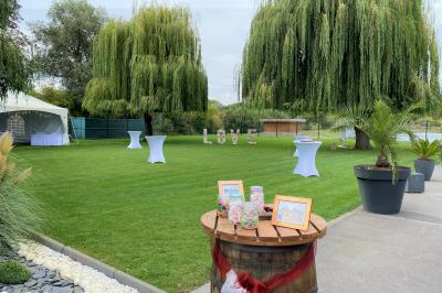 Table en bois décorée de bougies, fleurs et feuillage, entourée de chaises, sous une arche végétale dans une salle lumineuse.