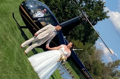 Table en bois décorée de bougies, fleurs et feuillage, entourée de chaises, sous une arche végétale dans une salle lumineuse.