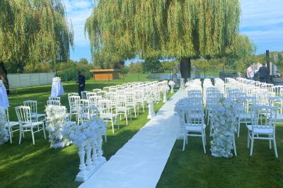 Table en bois décorée de bougies, fleurs et feuillage, entourée de chaises, sous une arche végétale dans une salle lumineuse.