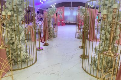 Table en bois décorée de bougies, fleurs et feuillage, entourée de chaises, sous une arche végétale dans une salle lumineuse.