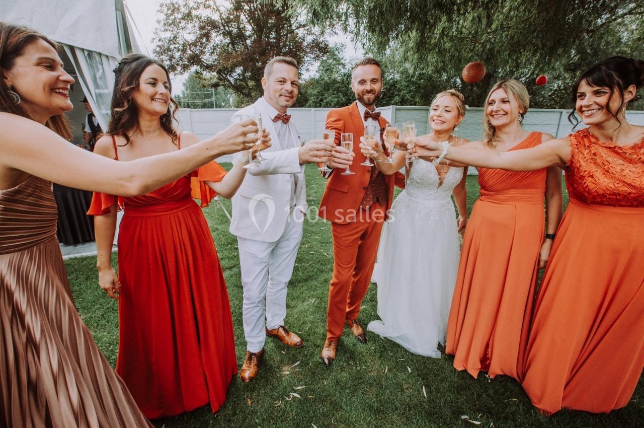 Un groupe de personnes élégamment vêtues trinque avec des verres dans un jardin lors d'une célébration.
