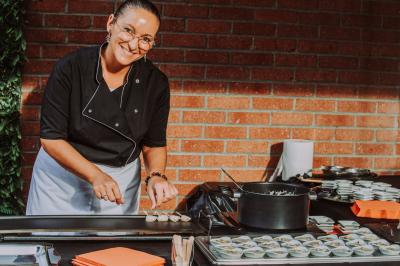 Table en bois décorée de bougies, fleurs et feuillage, entourée de chaises, sous une arche végétale dans une salle lumineuse.