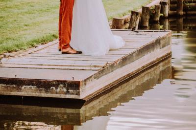 Table en bois décorée de bougies, fleurs et feuillage, entourée de chaises, sous une arche végétale dans une salle lumineuse.