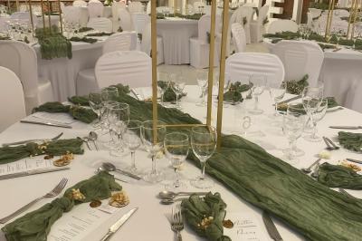 Table en bois décorée de bougies, fleurs et feuillage, entourée de chaises, sous une arche végétale dans une salle lumineuse.