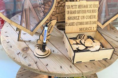 Table en bois décorée de bougies, fleurs et feuillage, entourée de chaises, sous une arche végétale dans une salle lumineuse.