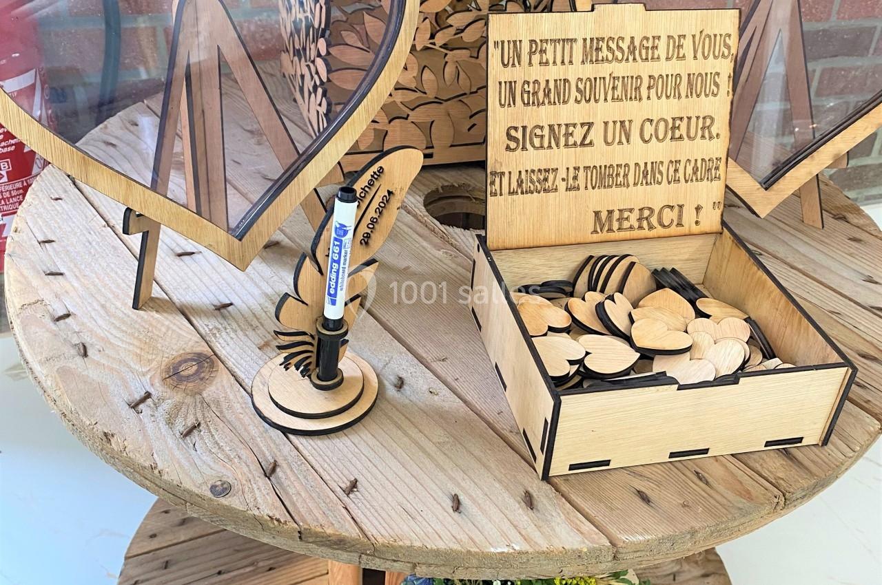 Boîte en bois pour messages de mariage, avec cœurs à signer, posée sur une table ronde en bois, décorée de fleurs.