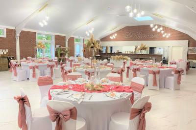 Table en bois décorée de bougies, fleurs et feuillage, entourée de chaises, sous une arche végétale dans une salle lumineuse.