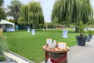 Table en bois décorée de bougies, fleurs et feuillage, entourée de chaises, sous une arche végétale dans une salle lumineuse.