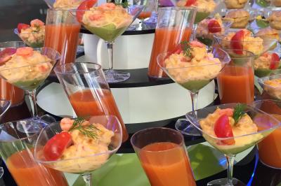 Table en bois décorée de bougies, fleurs et feuillage, entourée de chaises, sous une arche végétale dans une salle lumineuse.