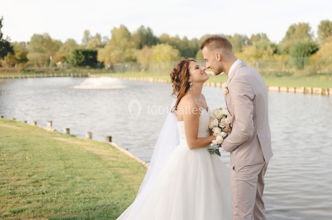 Un couple de mariés s'embrasse près d'un lac entouré de verdure par une journée ensoleillée.