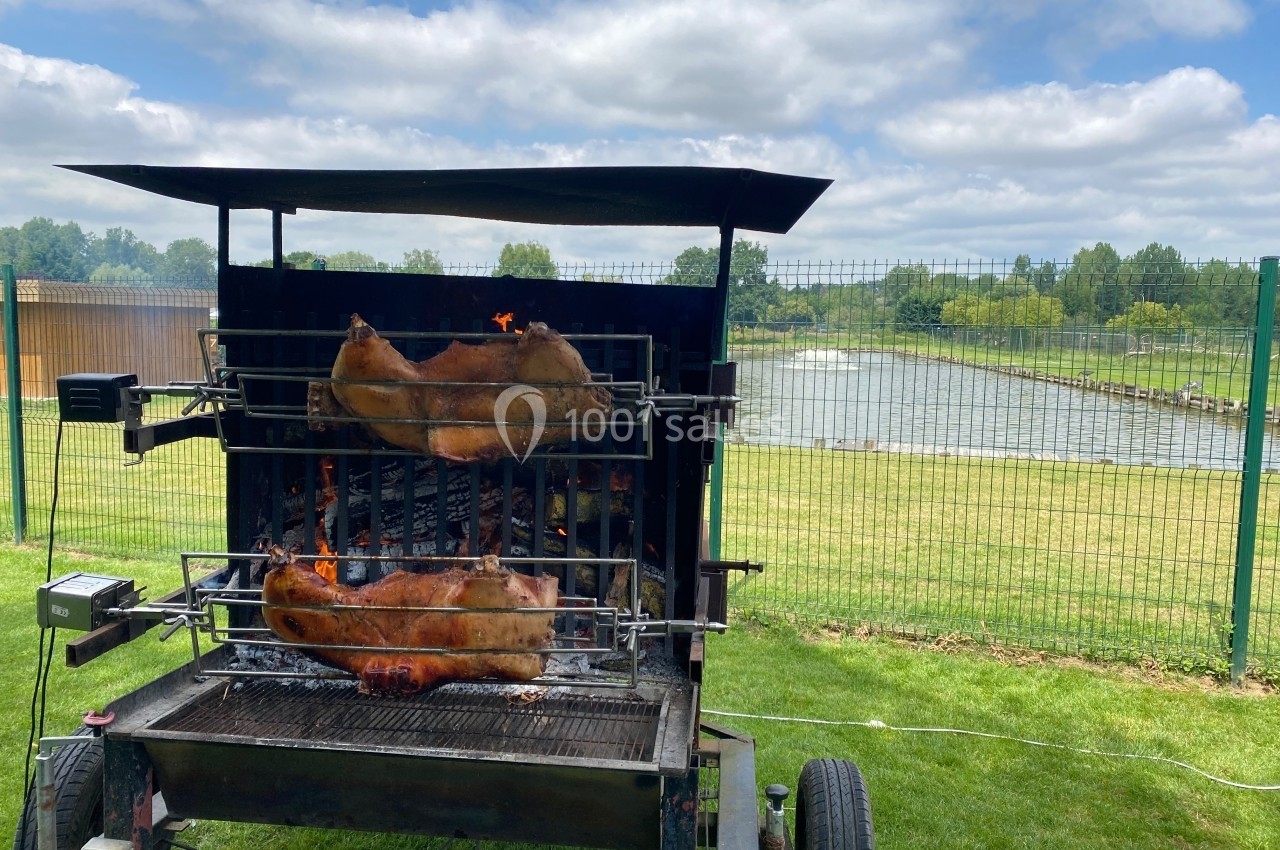 Deux pièces de viande rôtissent sur une broche au-dessus d'un barbecue, en plein air près d'un plan d'eau.