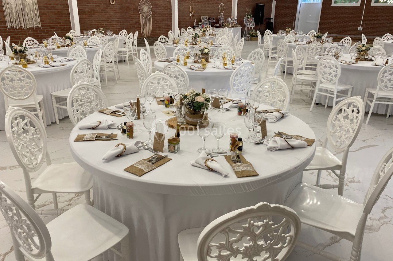 Salle de réception décorée avec des tables rondes blanches, nappes élégantes et chaises assorties, prête pour un événement.