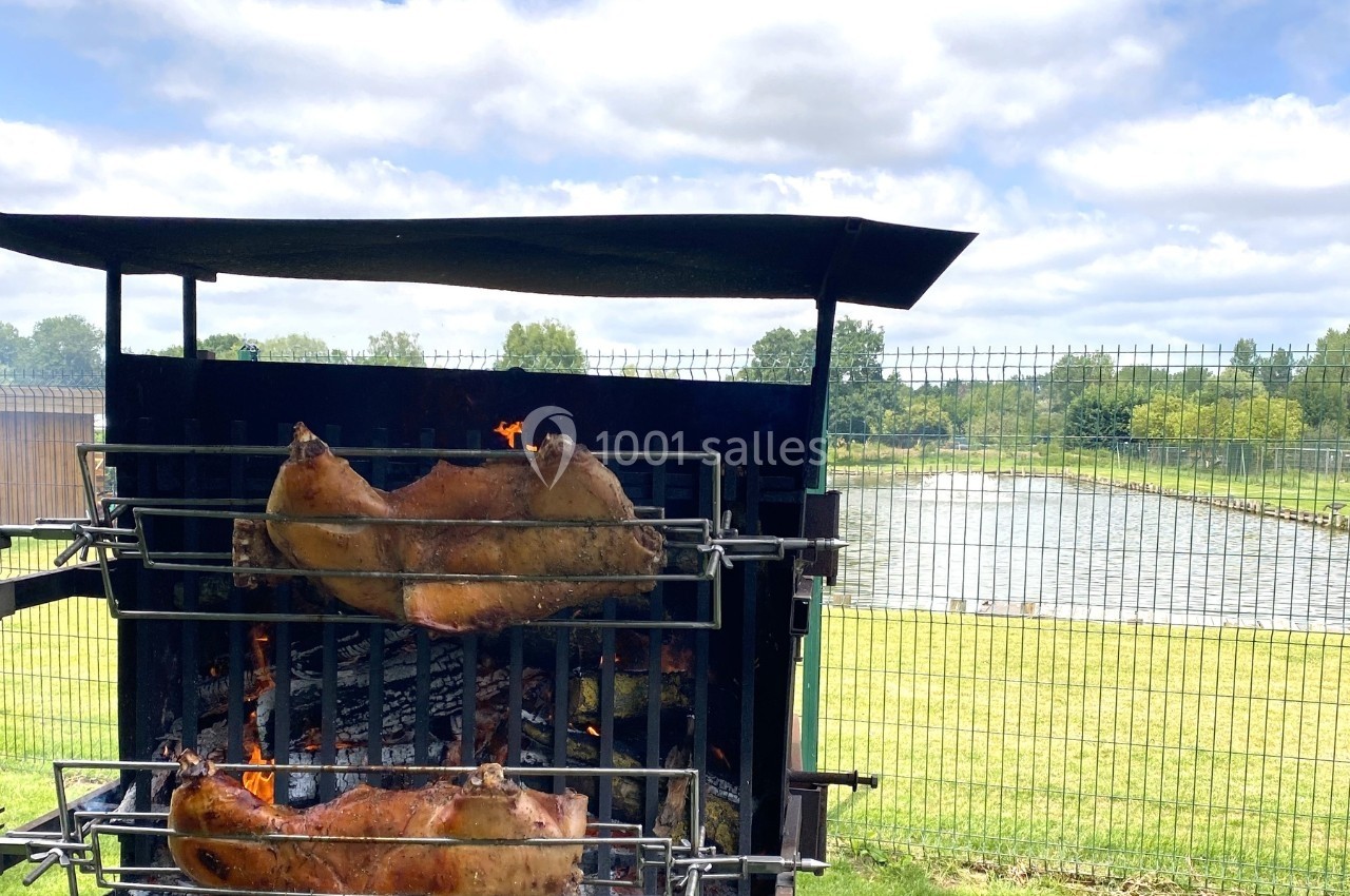 Deux porcelets rôtissent sur un barbecue en plein air, près d'un lac entouré de verdure.