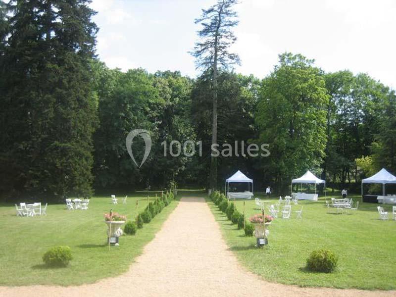 Allée centrale bordée de verdure menant à des tentes blanches dans un grand jardin arboré.