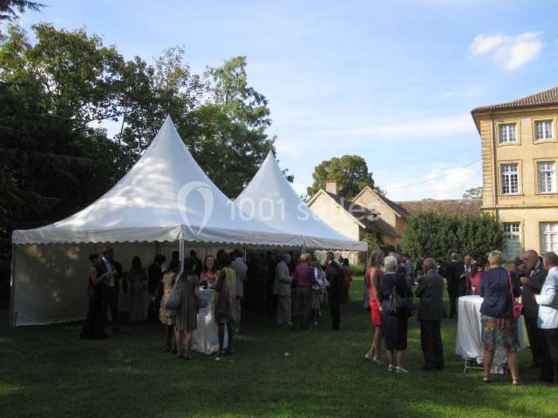 Groupe de personnes rassemblées sous des tentes blanches dans un jardin, près d'un bâtiment ancien.
