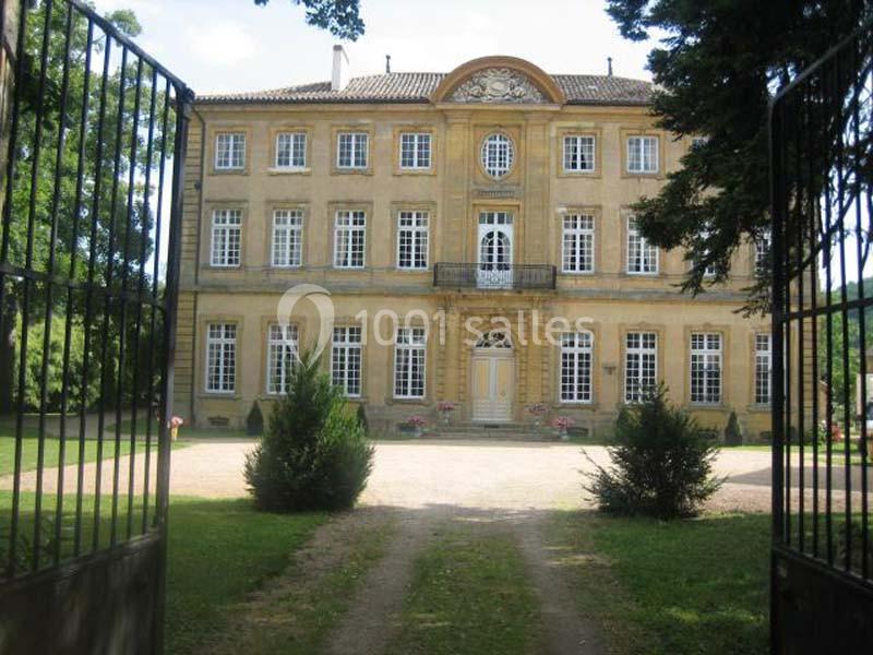 Façade d'un grand bâtiment ancien en pierre jaune, entouré d'arbres et visible à travers une grille ouverte.