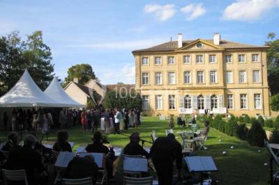 Chambre ancienne avec lit à baldaquin, fauteuil rouge, cheminée noire et murs tapissés de motifs verts.